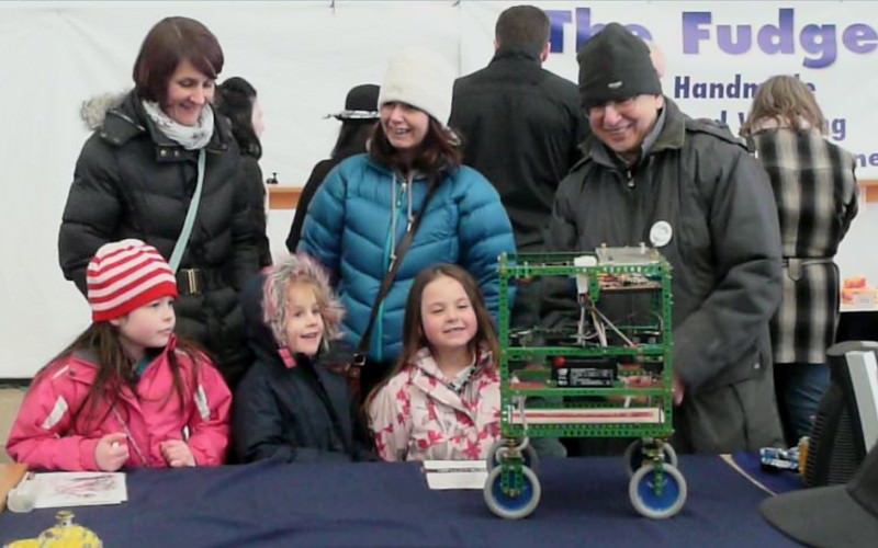 A family watches Alan Berman demonstrate his robot